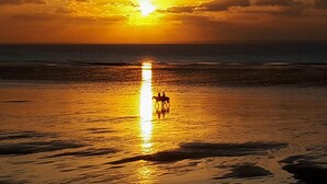 Escena de playa con atardecer, mar tranquilo y la silueta de una persona montando a caballo.