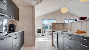 A modern kitchen with wooden cabinets, a coffee machine, and a dining area with a checkered tablecloth. - Nice home in Løkken with sauna (Løkken)