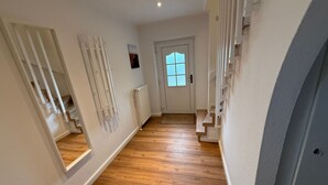 A hallway with wooden flooring, white walls, a white door with a window, and a white staircase. - Vacation home Queller 14, fenced garden, Wlan - Holiday home Queller 14 (Friedrichskoog)