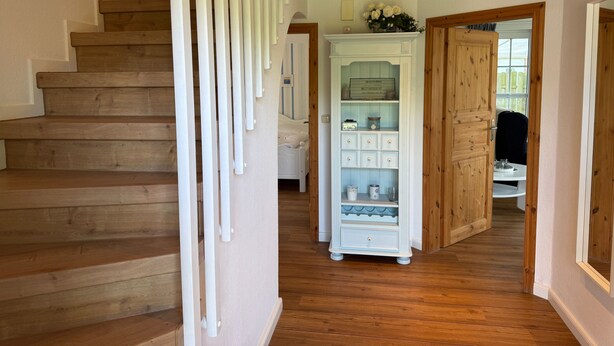 A wooden staircase leading to a bedroom with a white dresser and a small table. - Vacation home Queller 14, fenced garden, Wlan - Holiday home Queller 14 (Friedrichskoog)