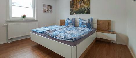 Un dormitorio con una cama, una ventana, un radiador y un cuadro en la pared.