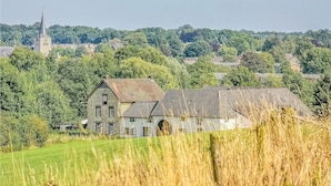 A stone building with a large arched doorway, surrounded by fields and trees.
