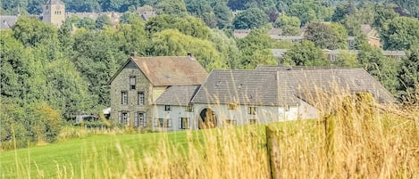 A stone building with a large arched doorway, surrounded by fields and trees.