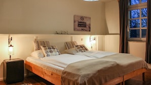 A bedroom with a wooden bed, two bedside lamps, a wall clock, and a window with curtains.