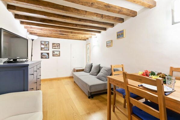 A room with a bed, a TV, a dining table with chairs, wooden beams on the ceiling, and artwork on the walls. - GuestHost - Comfortable and characteristic 55sqm apartment that can accommodate up to 4 people. Located on the mezzanine floor (two flights of stairs to access) of an ancient Florentine building, the apartment is located on the lower slope of Bardini Gar (Florence)