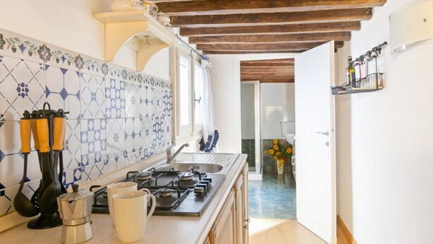 A kitchen with a tiled backsplash, wooden beams, a stove, and a sink.