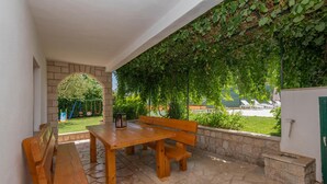 An outdoor patio with a wooden table and benches, surrounded by stone flooring and a green ivy-covered wall. - Amazing home in Runovic (Runovic)