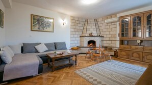 A cozy living room with a fireplace, a sofa, a dining table, and wooden cabinets. - Amazing home in Runovic (Runovic)