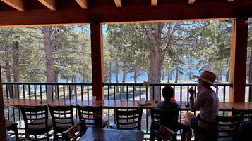 An outdoor seating area with wooden tables and chairs, overlooking a forested area.