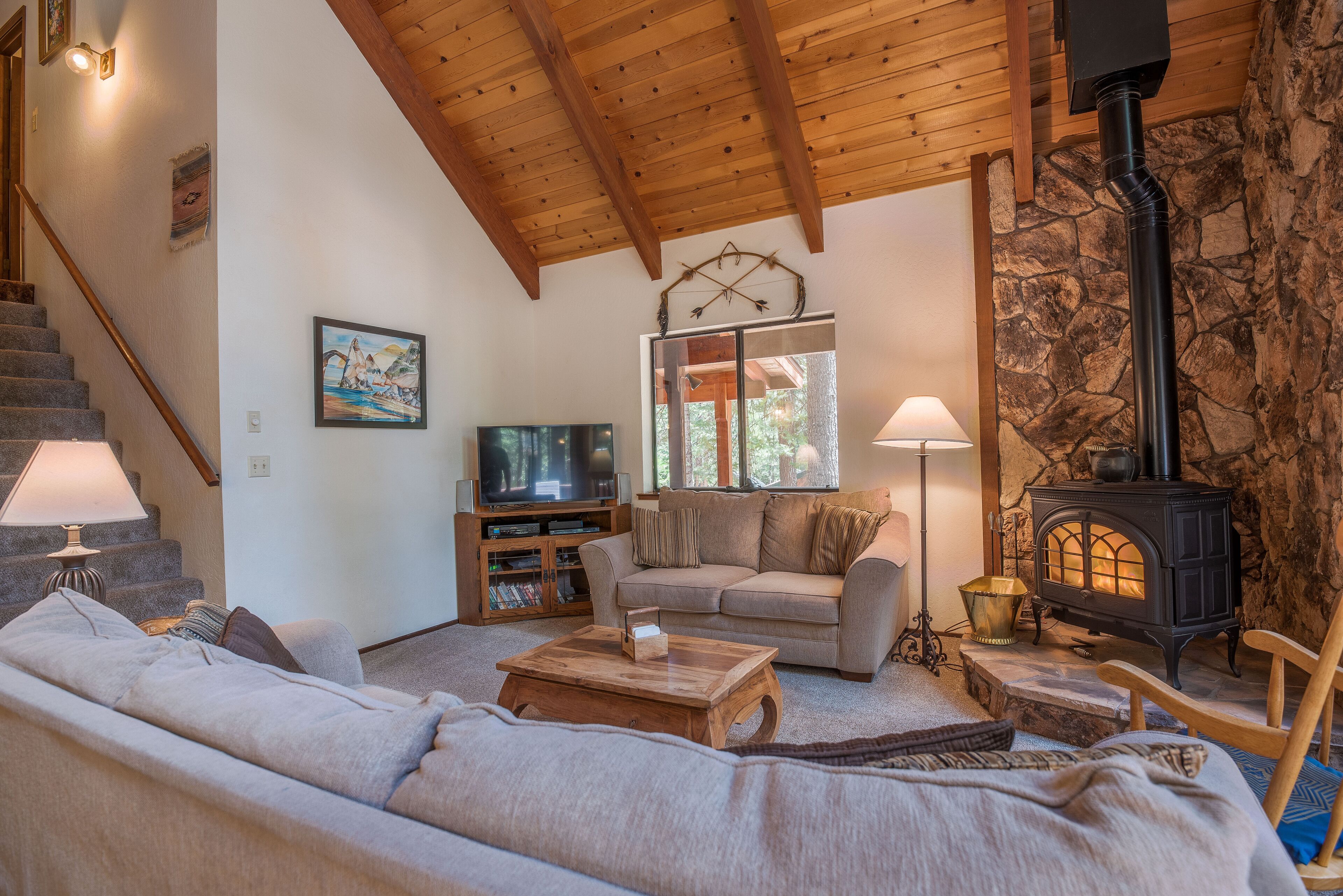 A cozy living room with a sofa, a coffee table, a fireplace, a television, and a staircase.