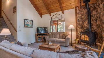 A cozy living room with a sofa, a coffee table, a fireplace, a television, and a staircase.