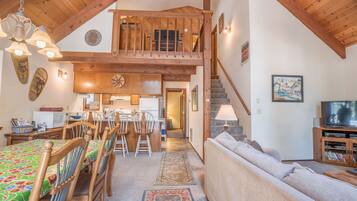 A spacious living area with a high ceiling, wooden beams, a dining area, and a staircase leading to an upper level.