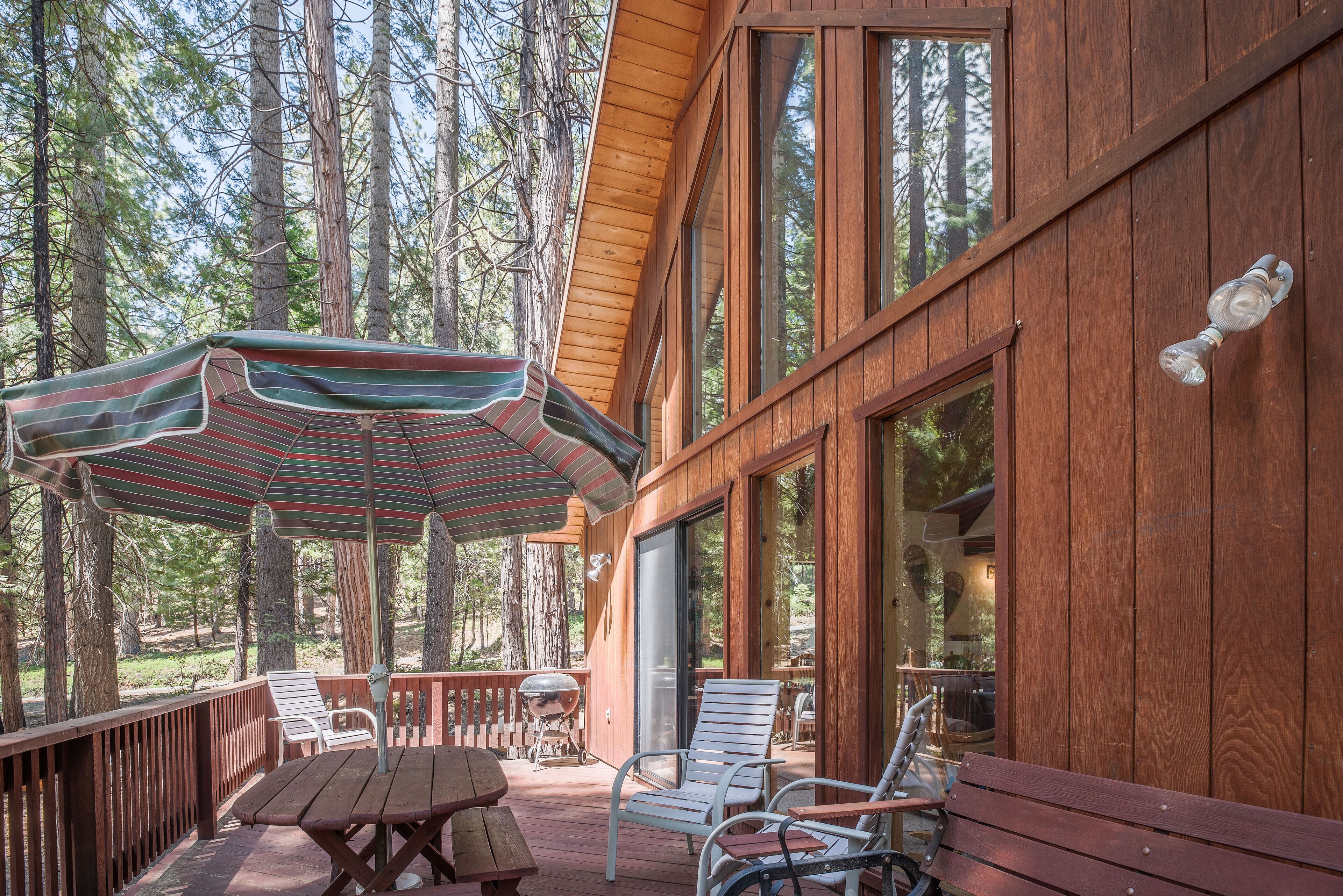 A wooden deck with outdoor seating, including a picnic table and chairs, and a large umbrella.