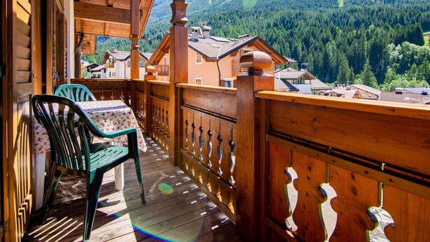 Un balcone in legno con un tavolo e sedie, affacciato su un paesaggio montuoso con case.