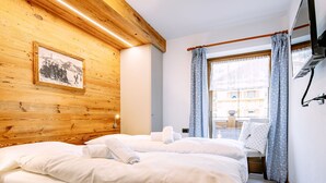 Camera d'albergo con soffitto in legno, un letto con lenzuola bianche, un piccolo tavolo con una sedia e una finestra con tende.