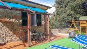 Un bâtiment en pierre doté d’un patio carrelé, d’un espace extérieur aménagé pour s’asseoir et d’une structure de jeux.
