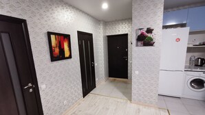 A hallway with patterned wallpaper, a black door, a white refrigerator, and a washing machine in the kitchen area. - Have your own privacy with total comfort at a very low price. (Kyiv)