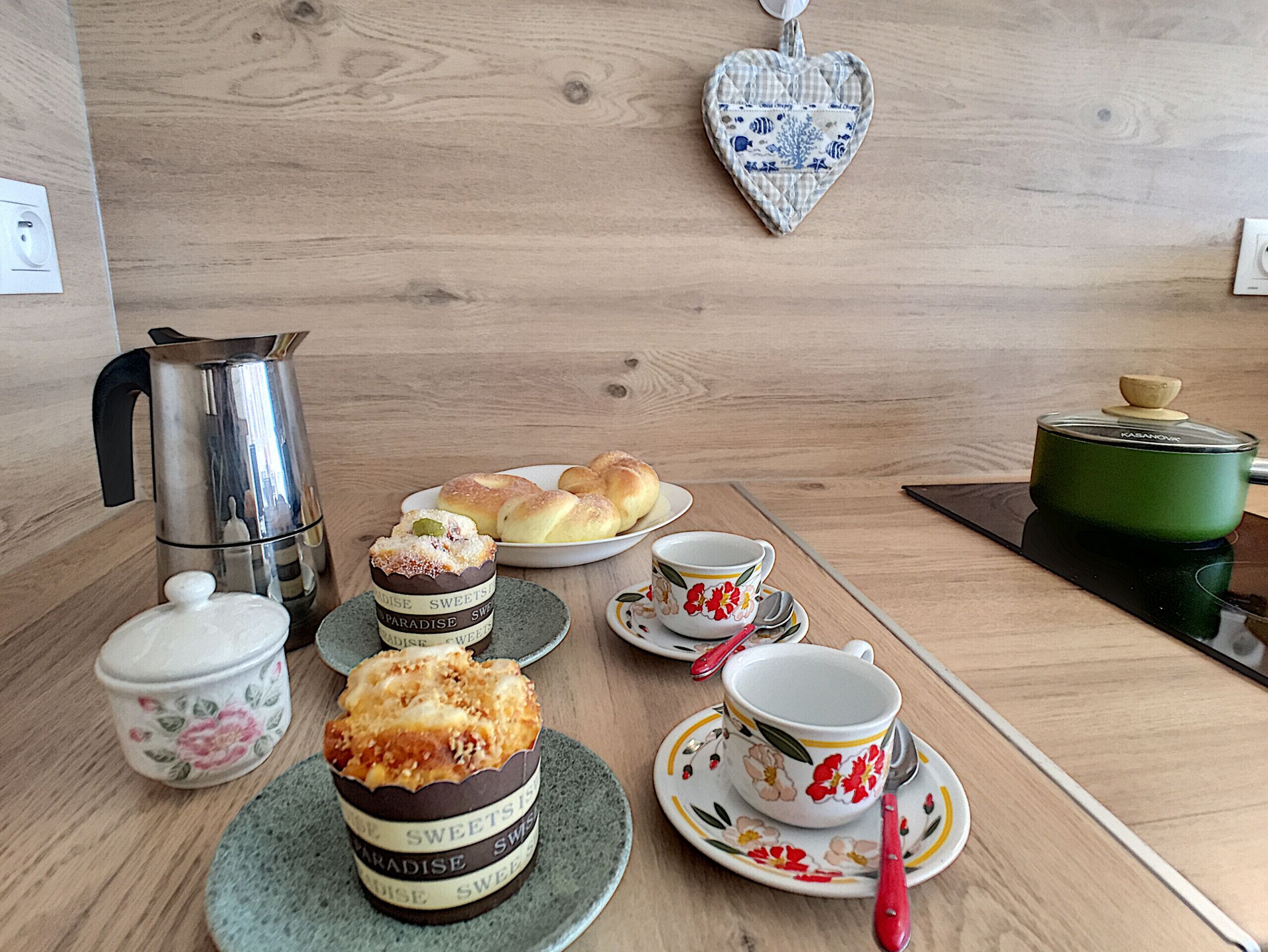 A wooden table with a coffee pot, pastries, a teapot, and a heart-shaped decoration.