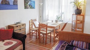 Una sala de estar acogedora con una mesa de comedor, muebles de mimbre y vista al mar a través de cortinas translúcidas.