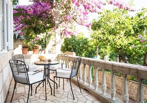 Een terras met een ronde tafel en twee stoelen, een stenen vloer en een balustrade.