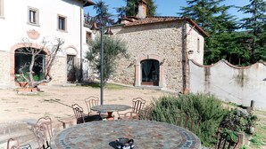Un patio con una mesa mosaicos redonda, sillas de metal y un edificio de piedra con tejado de tejas.