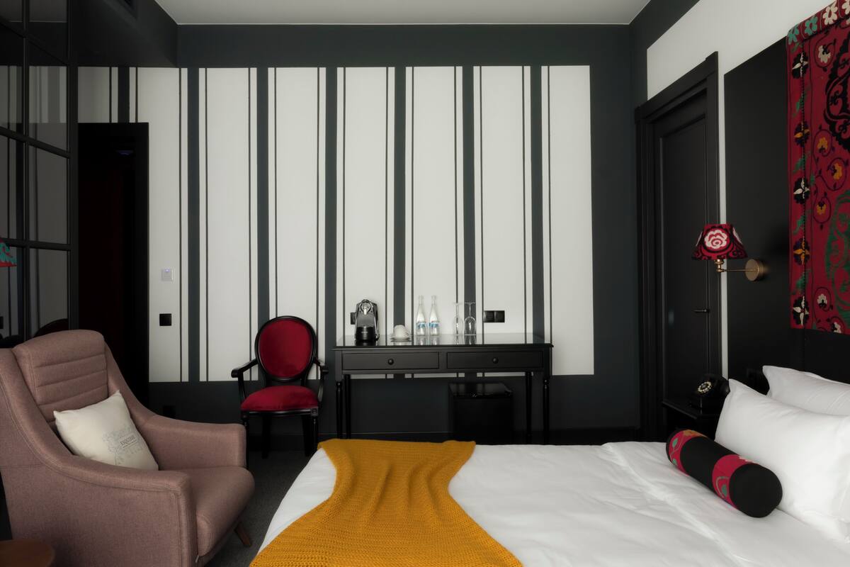 Une chambre d’hôtel comprenant un lit, un bureau, une chaise, une armoire et un mur d’accent de couleur rouge.