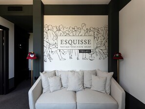 A modern hotel lobby with a large wall mural depicting a crowd, a sofa with multiple cushions, and two floor lamps. - Esquisse Boutique Hotel (Telavi)