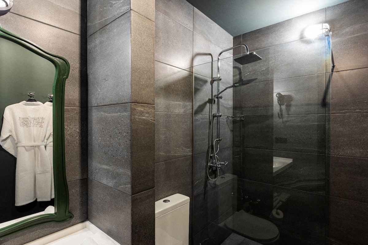 A bathroom with a glass-enclosed shower, a toilet, and a mirror with a green frame.