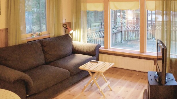 Ein gemütliches Wohnzimmer mit einer Couch, einem kleinen Tisch und Blick auf eine Holzterrasse durch große Fenster.