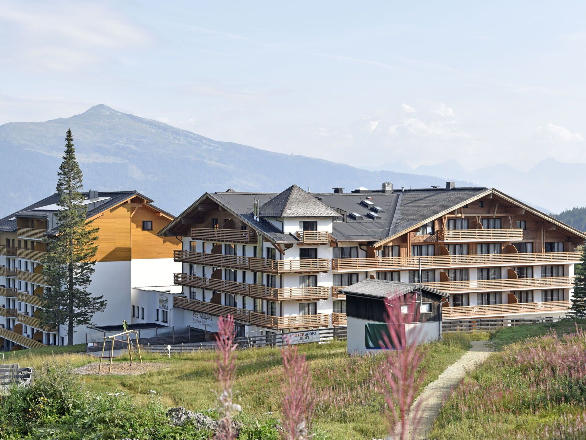 Ein mehrstöckiges Hotel mit Balkonen, einem Restaurant und einer Seilbahn im Hintergrund.
