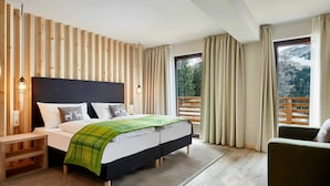 A modern bedroom with a wooden slat wall, a bed with a green blanket, a nightstand, a chair, and a view of a snowy landscape through a window. - Beautiful apartment for 6 people with WIFI, pool, TV, balcony, pets allowed and panoramic view (Feichtinger)