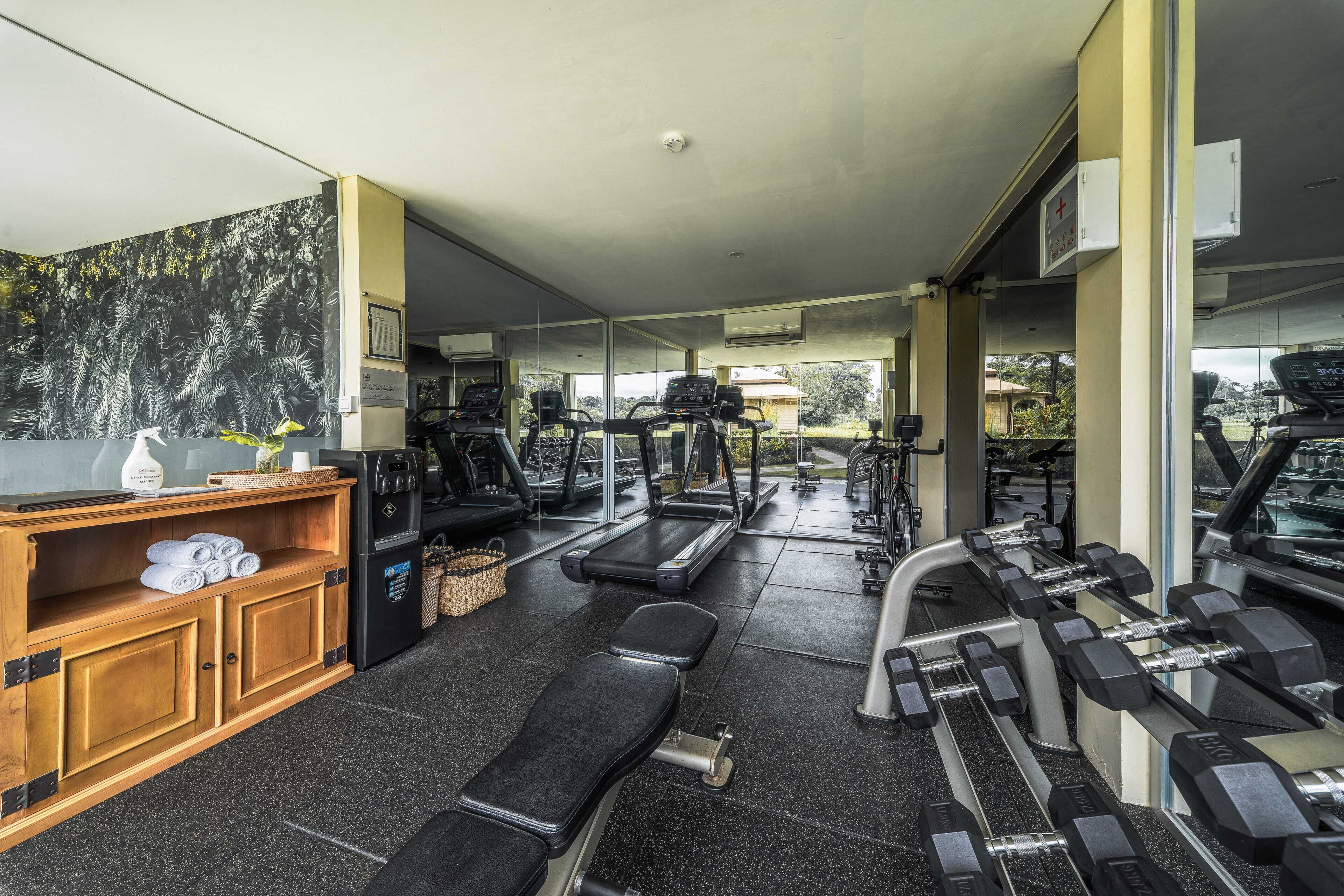 A gym with treadmills, dumbbells, and a wooden cabinet with towels.