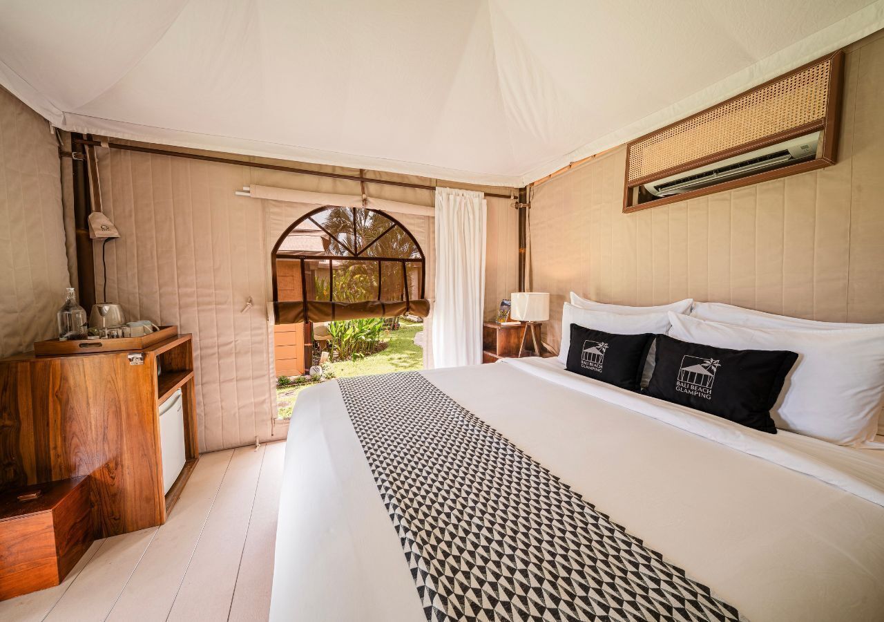 Un dormitorio con una cama grande, una mesita de noche de madera, una pequeña mesa y una ventana con cortinas.
