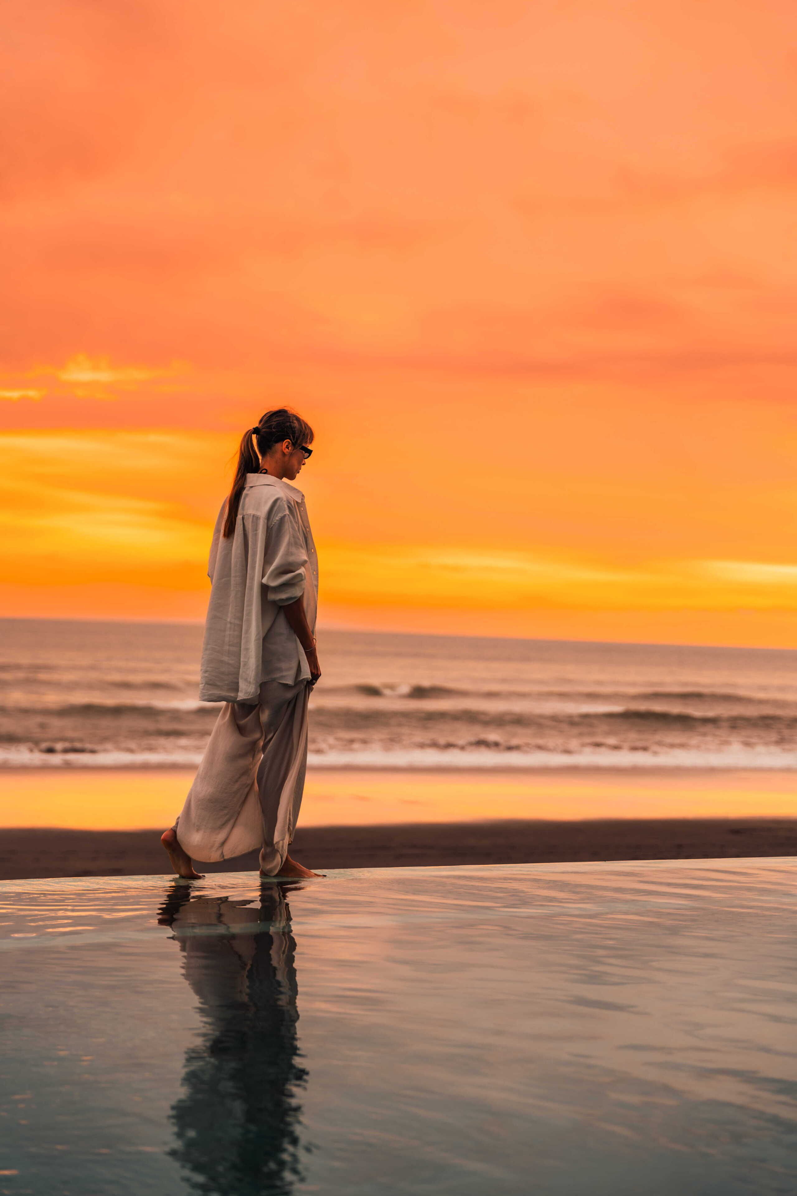 A person standing on a reflective surface by the ocean at sunset.