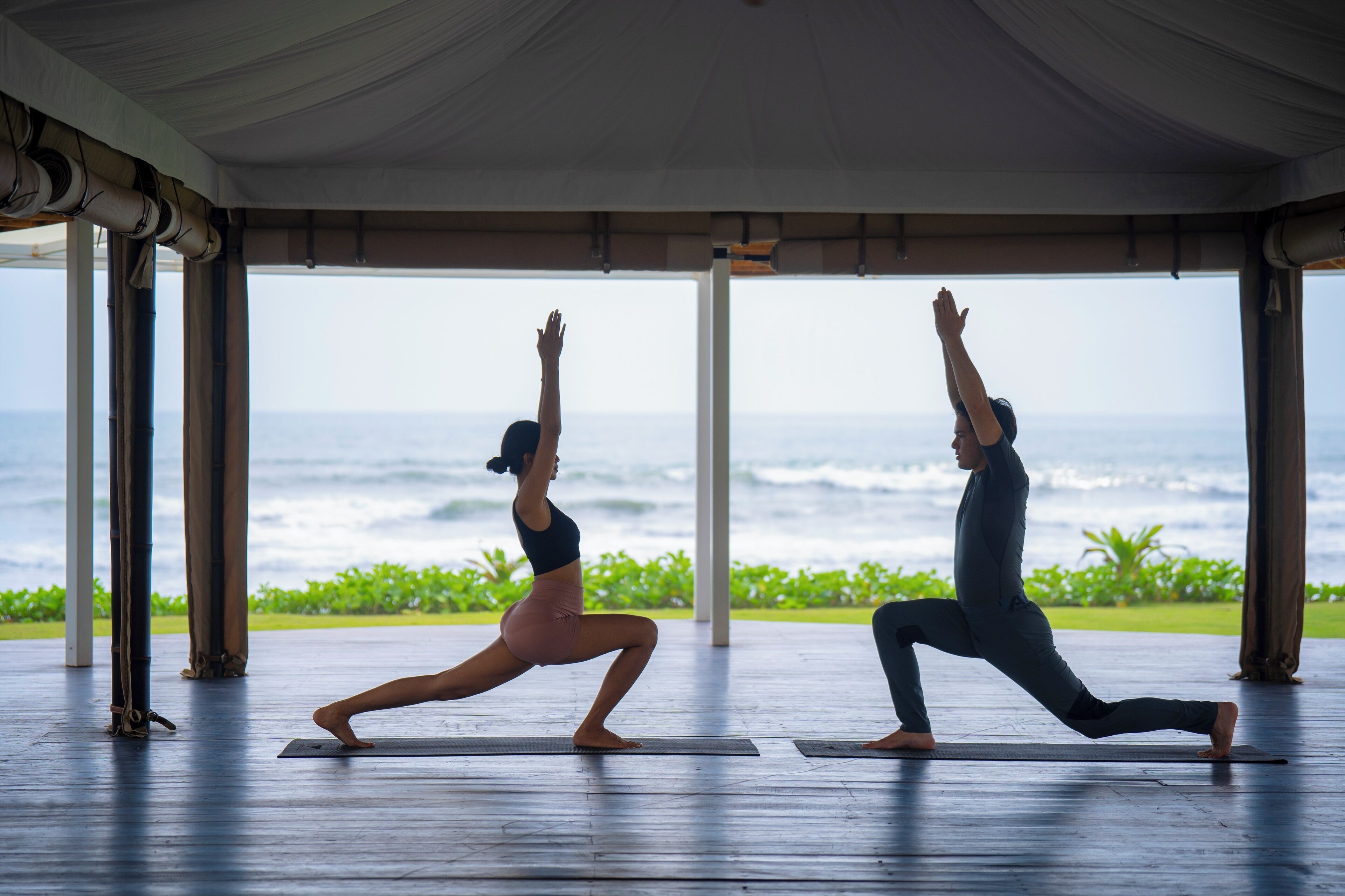 Two people performing yoga in a spacious room with a view of the ocean.