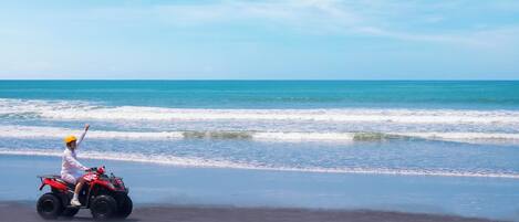Una persona conduce un vehículo todo terreno rojo sobre una playa, con el océano al fondo.
