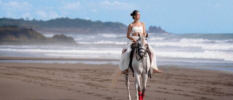 Una persona montando a caballo en una playa, con olas al fondo.