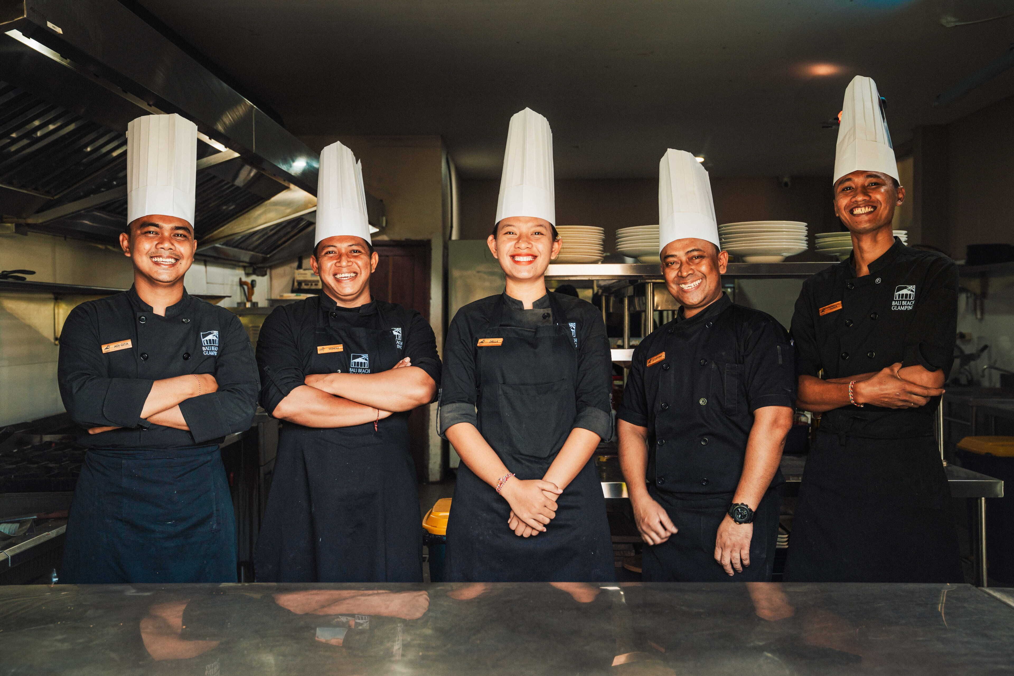 A group of chefs standing in a kitchen with stainless steel surfaces and professional kitchen equipment.