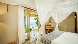 A bedroom with a bed, a wooden nightstand, a small table, and a view of the ocean through a glass door. - Bali Beach Glamping (Tabanan)