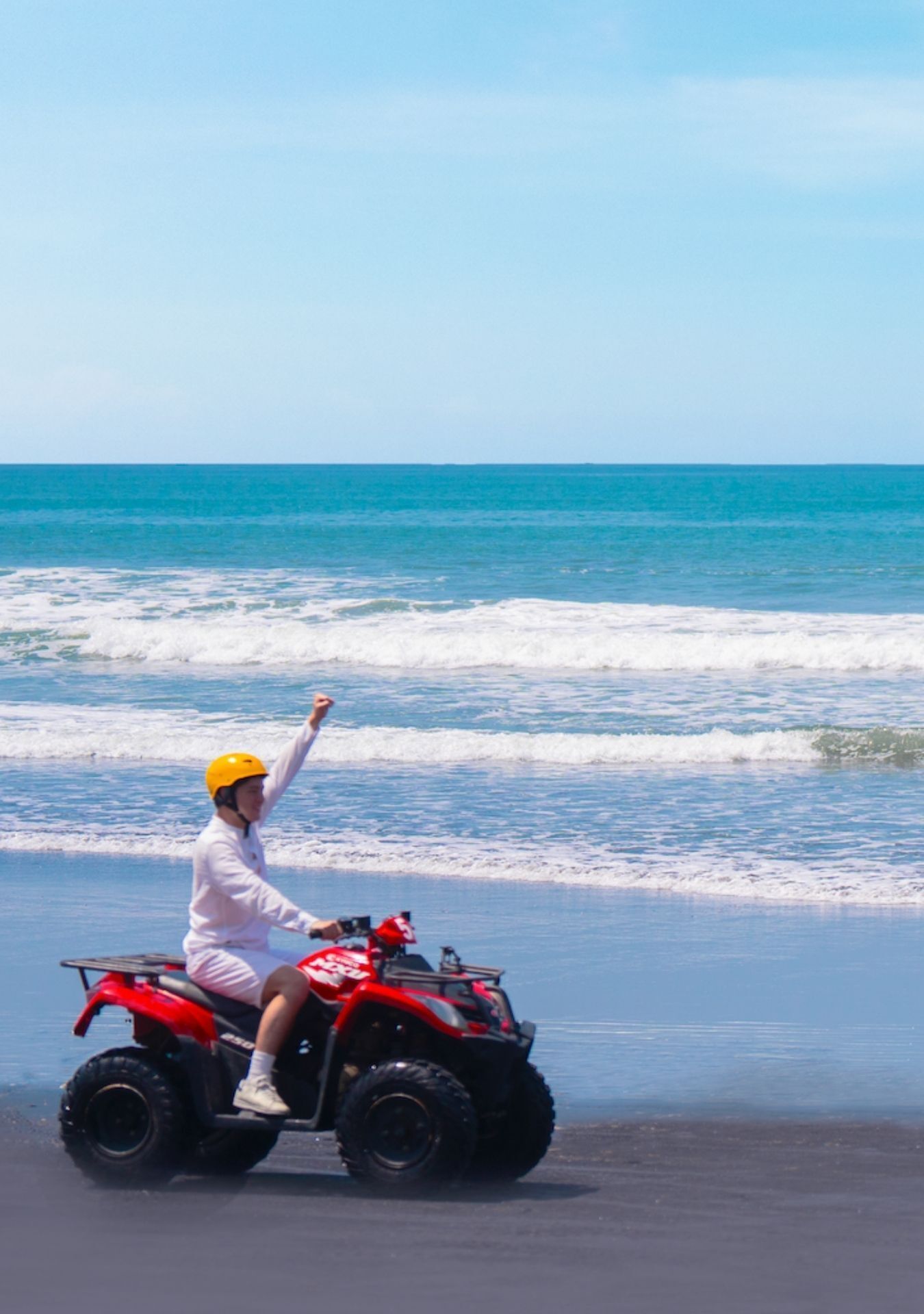 A person on a red ATV on a beach with ocean waves in the background.