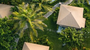 An aerial view of a resort with multiple bungalow-style buildings, surrounded by lush greenery and palm trees. - Bali Beach Glamping (Tabanan)