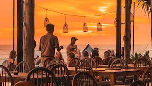 An outdoor dining area with tables and chairs, overlooking the ocean at sunset. - Bali Beach Glamping (Tabanan)