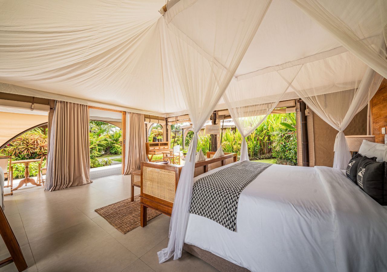 Une chambre à coucher avec un lit à baldaquin, un bureau en bois et une vue sur la verdure environnante.