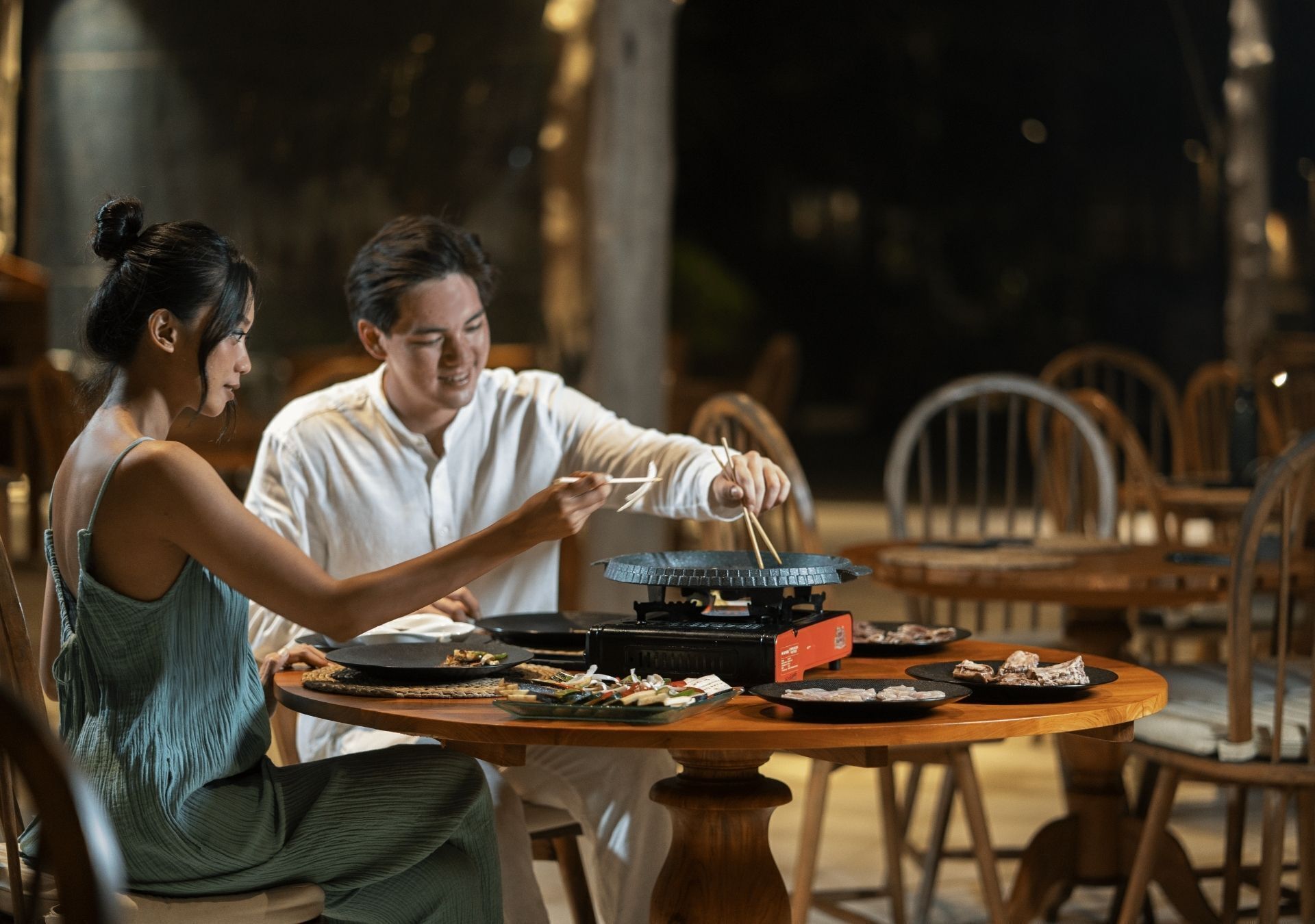A dining table with a grill, plates, and chopsticks.