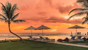 A beachside resort with lounge chairs, umbrellas, and a palm tree. - Bali Beach Glamping (Tabanan)