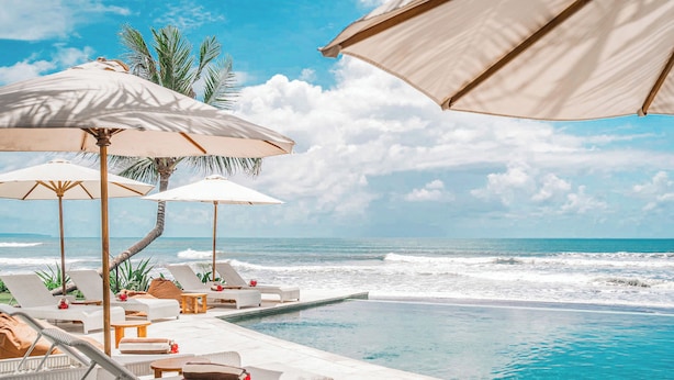A poolside area with lounge chairs, umbrellas, and a view of the ocean. - Bali Beach Glamping (Tabanan)