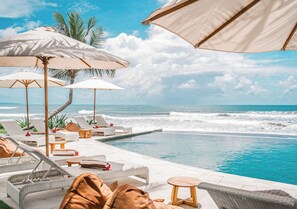 A poolside area with lounge chairs, umbrellas, and a view of the ocean. - Bali Beach Glamping (Tabanan)