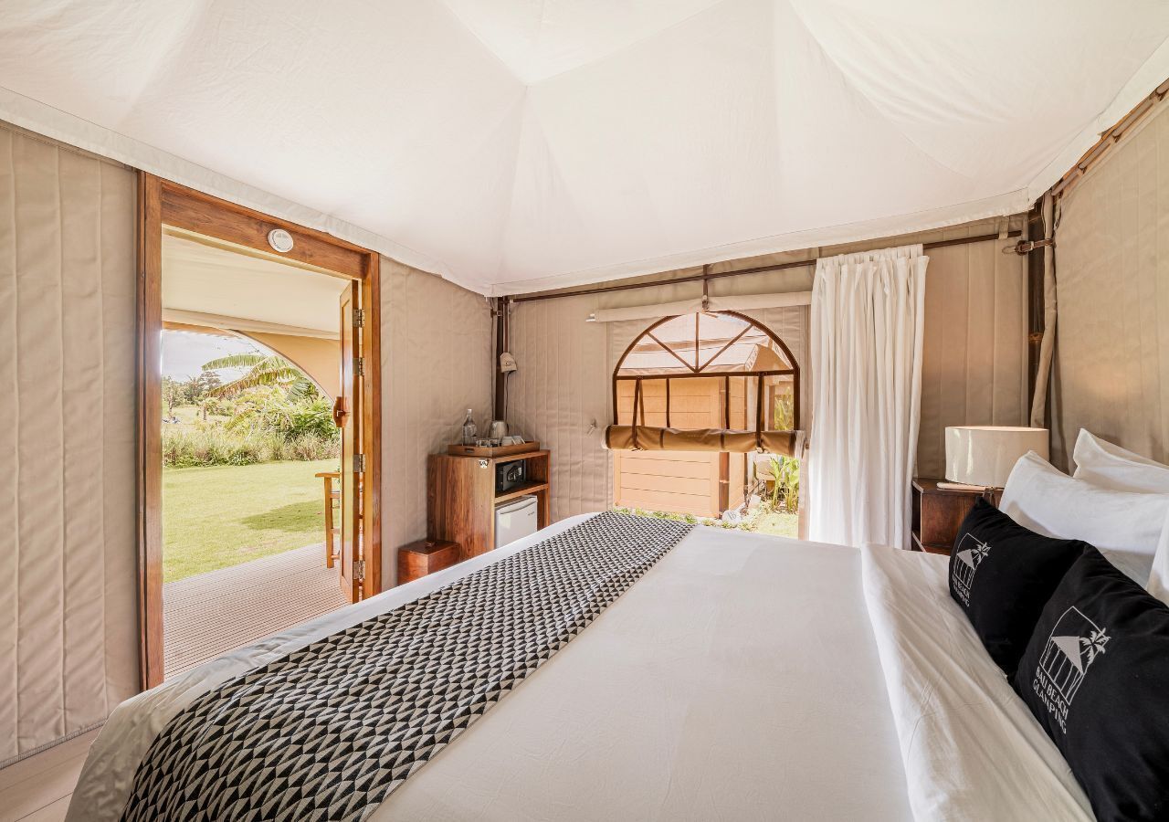 A tented room with a bed, a desk, and a view of the outdoors.