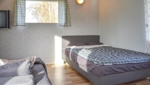 Ett sovrum med en säng, en soffa, ett fönster med gardiner och en väggmonterad lampa.