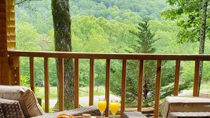 A wooden deck with wicker furniture and a table set with fruits and a drink, overlooking a forested landscape. - Big Kahuna Lodge 3 Bedroom Cabin by RedAwning (Sevierville)